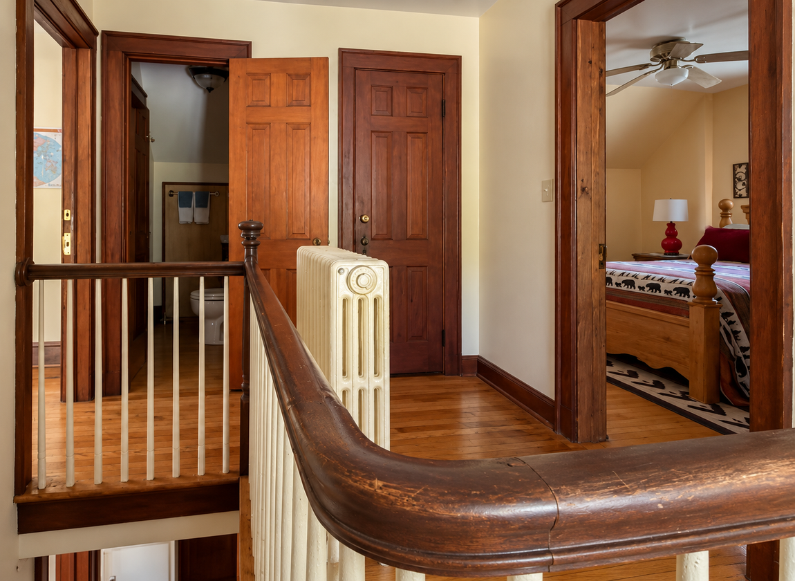 Upstairs hallway at Red Fox Townhouse featuring hardwood floors, wooden doors, staircase railing and entrance to a bedroom.