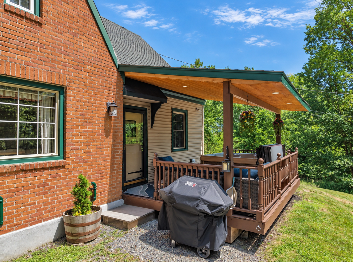 Covered deck at Red Fox Townhouse in Windham, NY, featuring a private hot tub, barbecue grill and wooded surroundings.