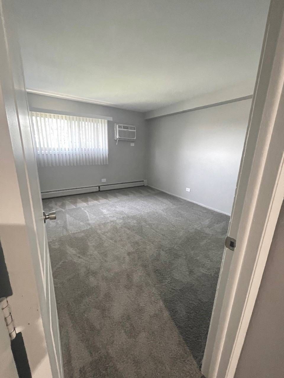 Empty carpeted bedroom with gray walls, a window, and a wall-mounted air conditioner.