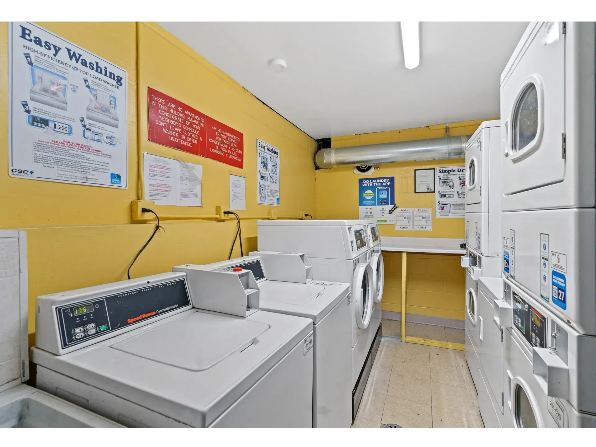 Laundry room with coin-operated washers and dryers against a yellow wall