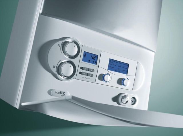 A close-up of a white wall-mounted boiler control panel with digital displays, circular adjustment knobs, and buttons.