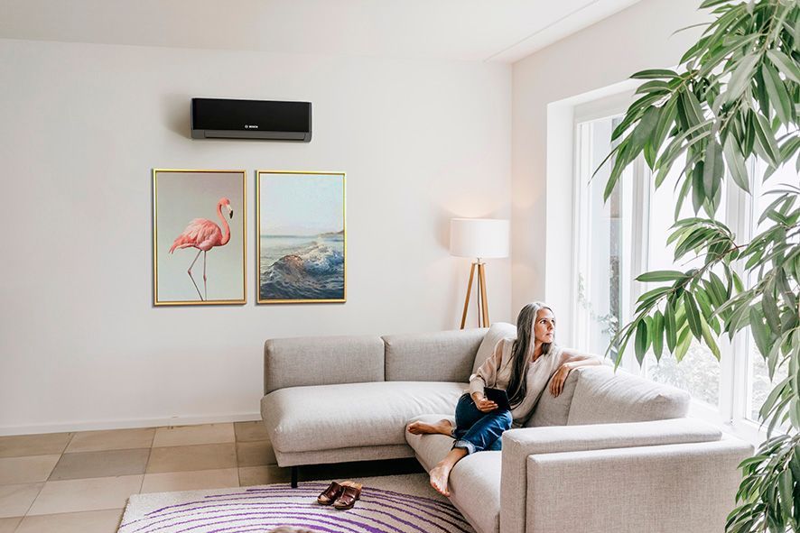 A person relaxes on a light-colored sectional sofa in a bright room with wall art and a large indoor plant.