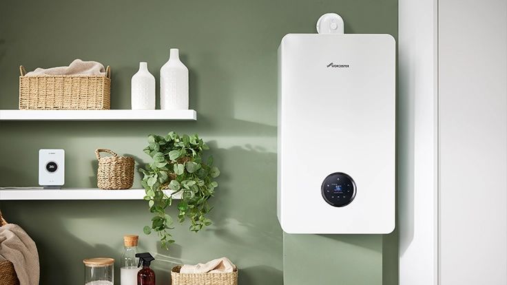 A wall-mounted white Worcester Bosch boiler in a green room with shelves containing home decor and a plant.