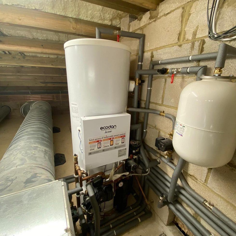 An Ecodan heat pump unit with a white storage cylinder and expansion vessel in a residential loft space.