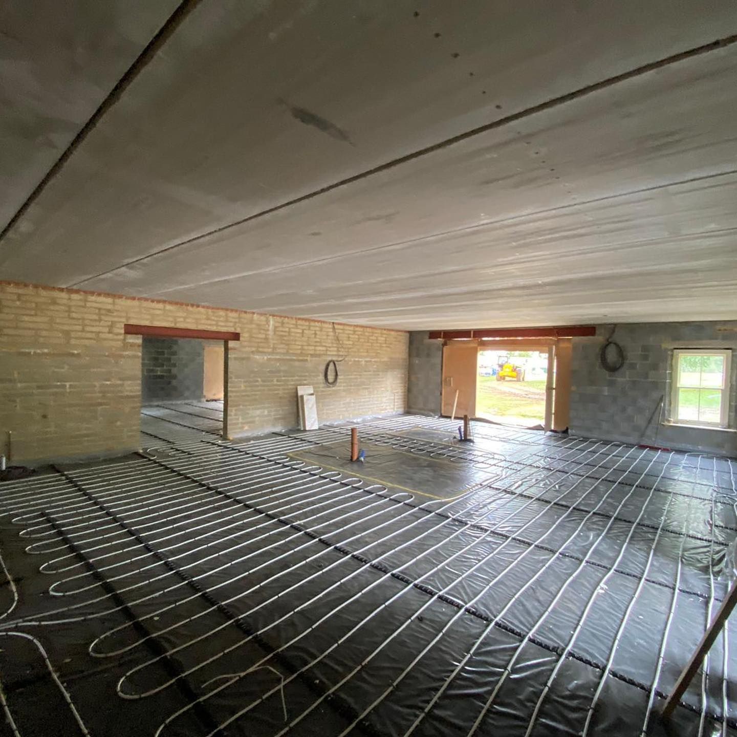 A room under renovation with radiant heating tubing installed on a black vapor barrier over the subfloor.