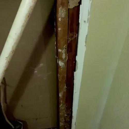 Wooden trim on a wall with peeling paint, next to a pipe.