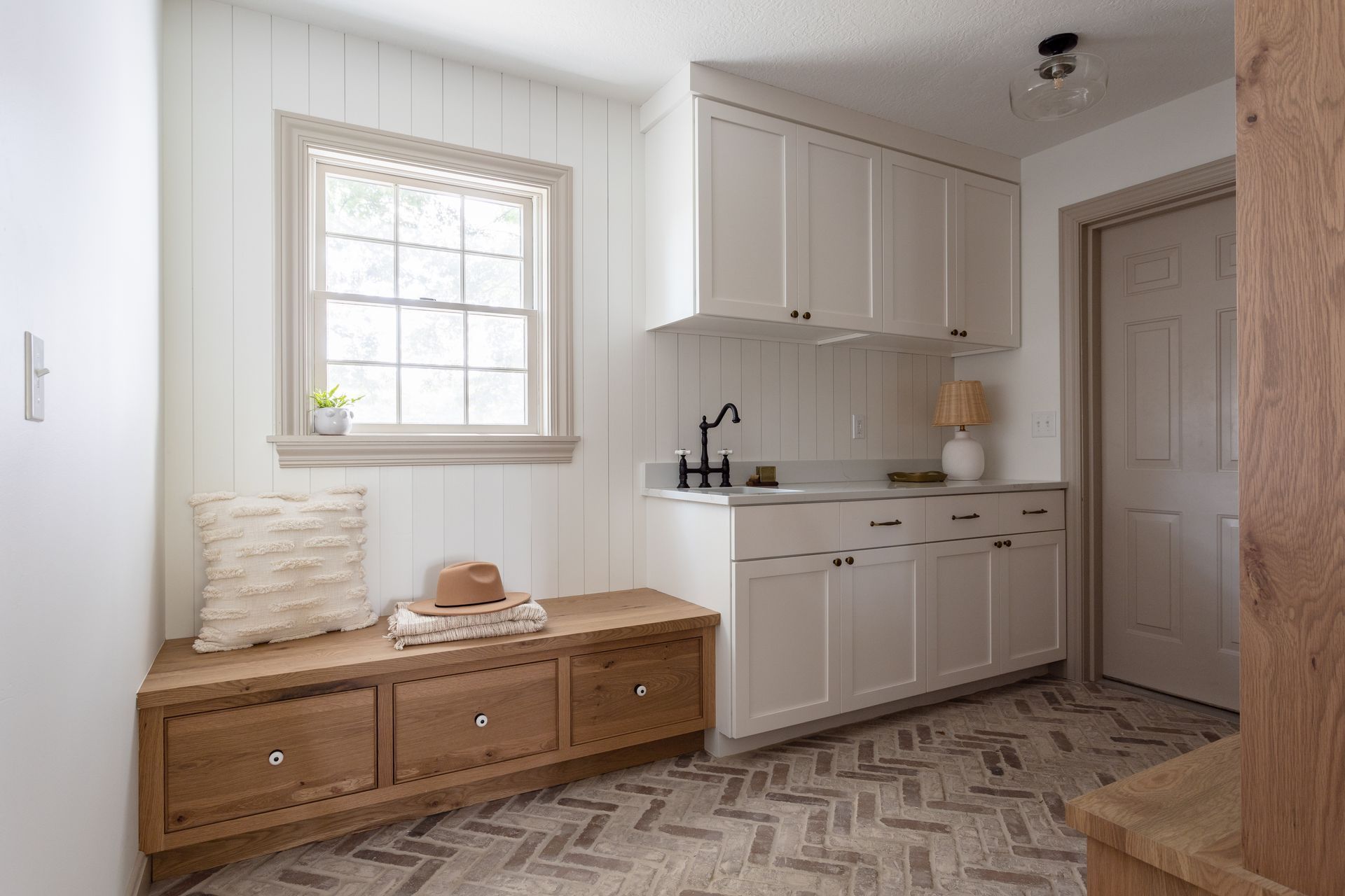 Laundry room with white cabinets, wood bench, window, and patterned tile floor.