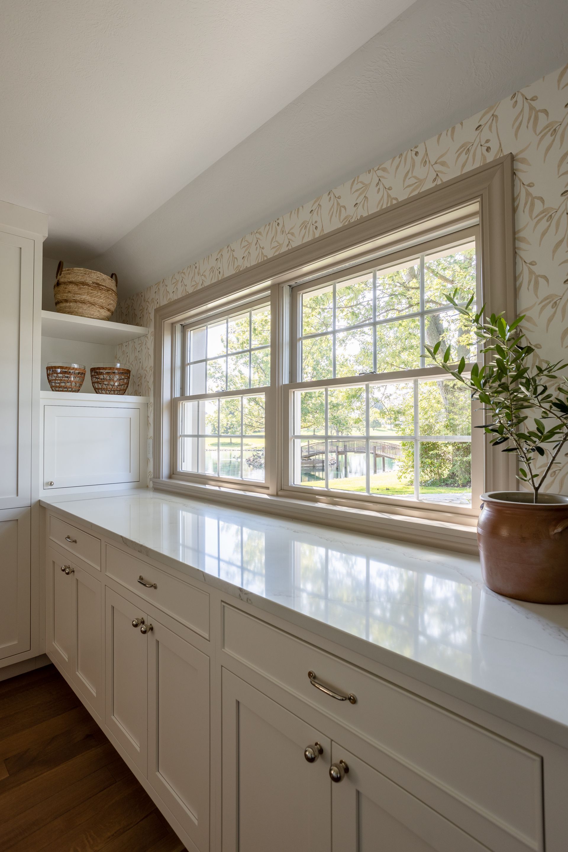 White kitchen counter with cabinets below a double-hung window; a plant sits on the right.