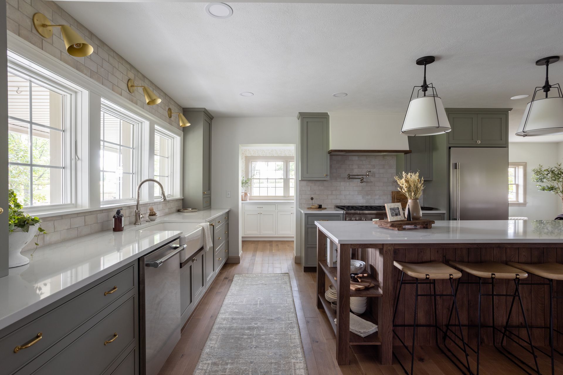 Kitchen with sage green cabinets, white countertops, and a wooden island with barstools.