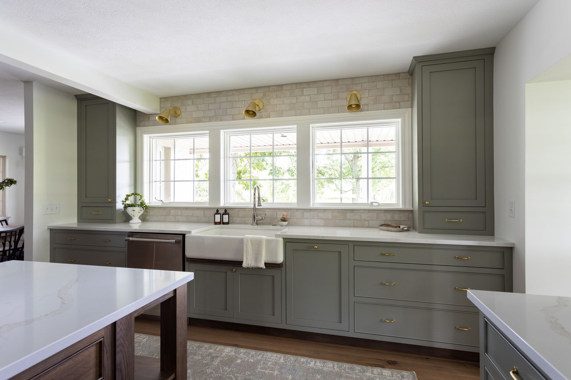 Kitchen with green cabinets, white countertops, three windows, and a farmhouse sink.