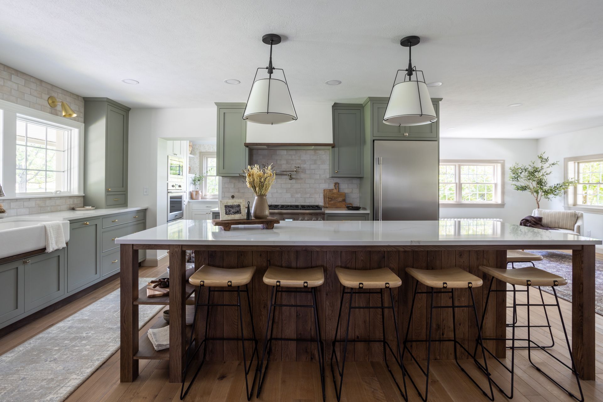 Modern kitchen with green cabinets, white countertops, and a large island with bar stools.