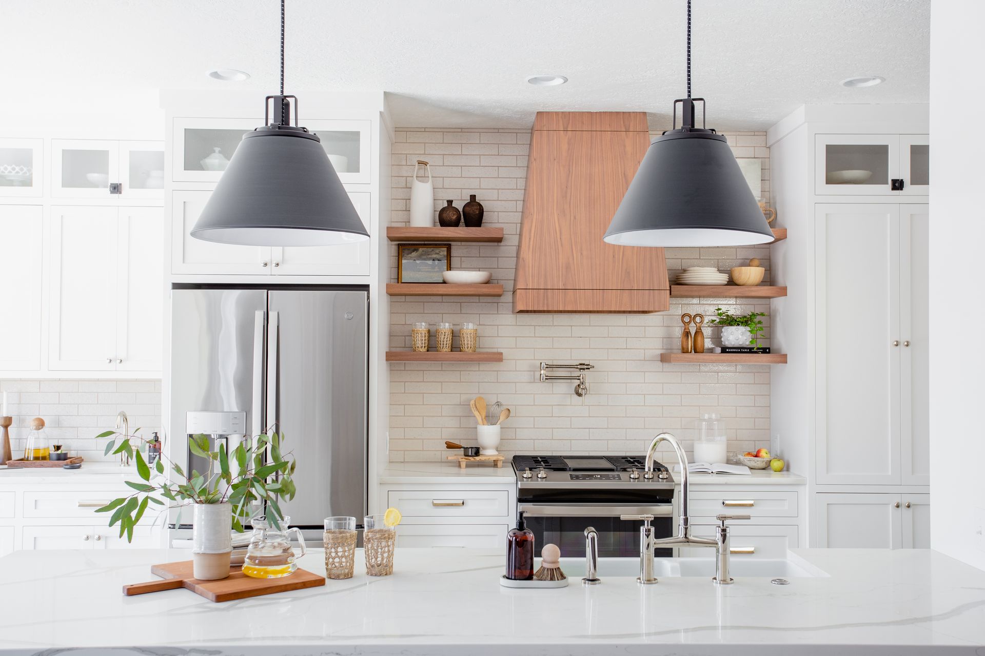 White kitchen with stainless steel appliances, wood shelves, and two gray pendant lights.