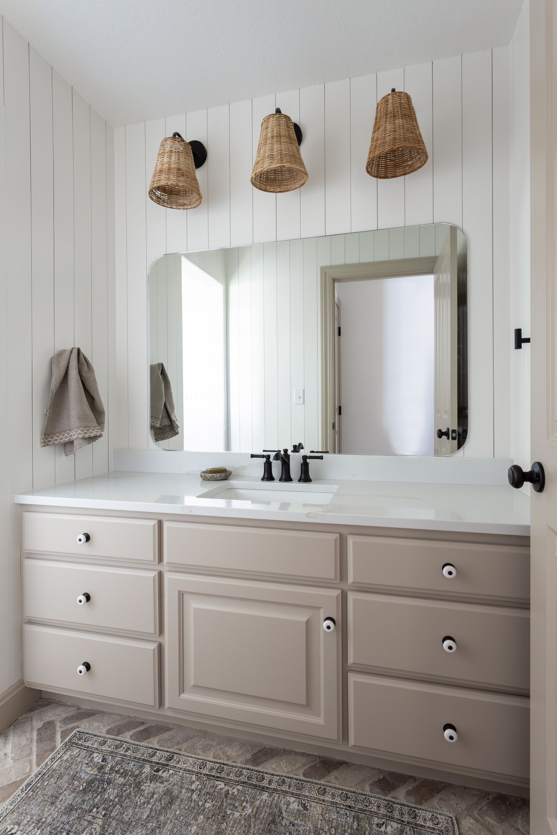 Bathroom vanity with beige cabinets, a large mirror, and three woven light fixtures.