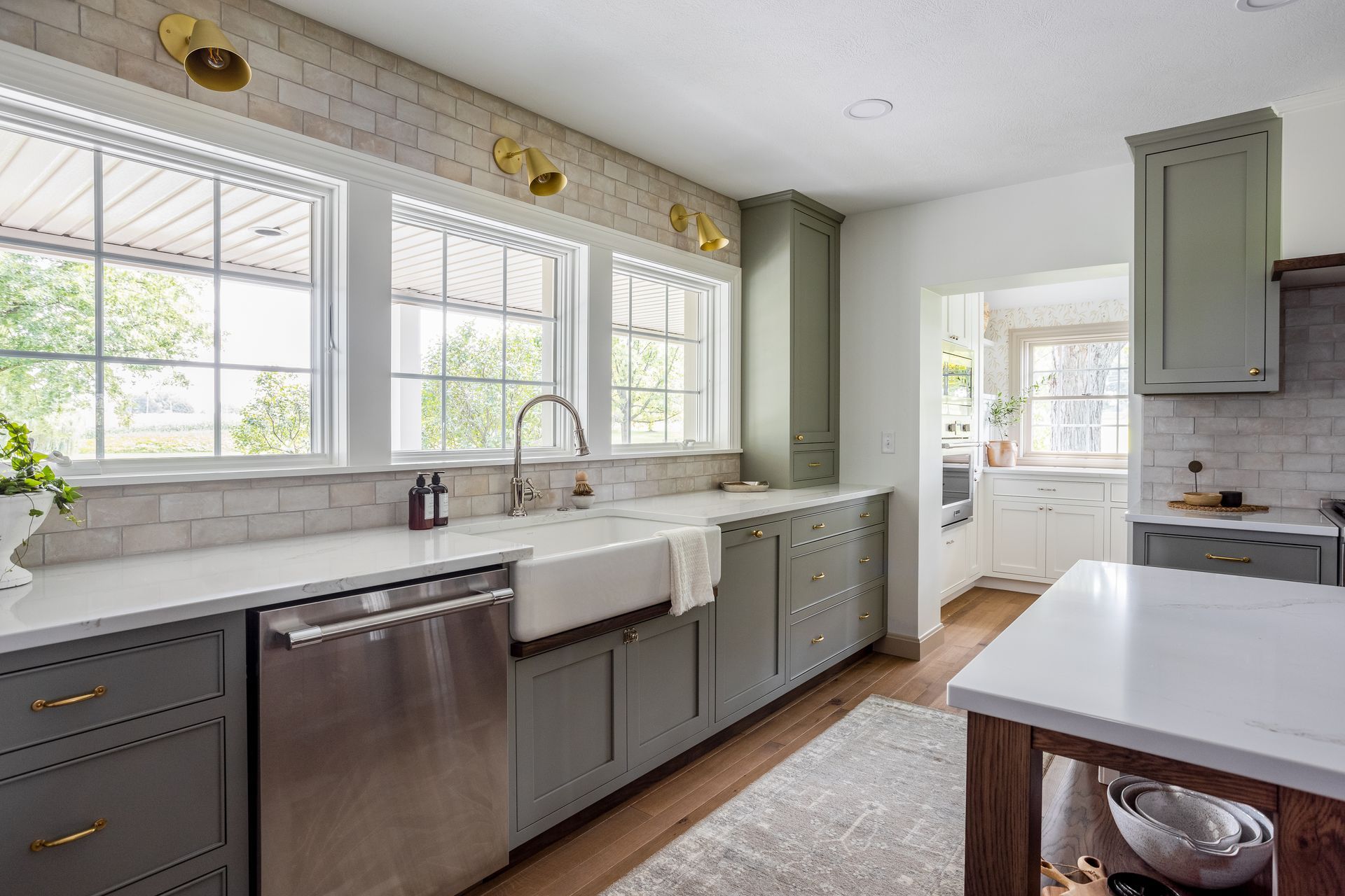 Kitchen with sage green cabinets, white countertops, and stainless steel appliances. Three windows over the sink area.