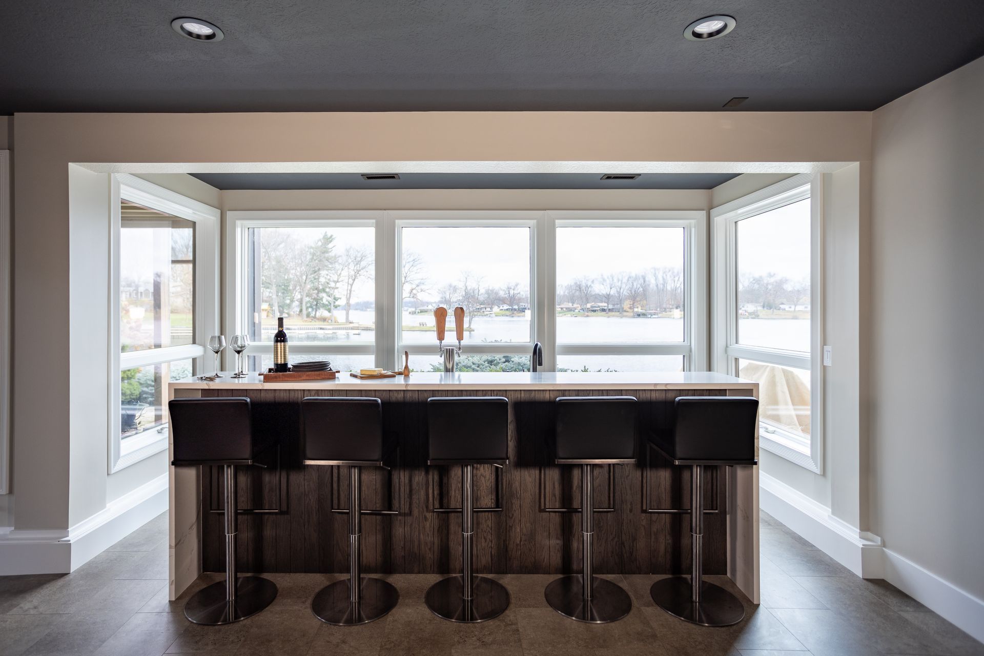 Bar with stools in front of large windows overlooking a body of water.
