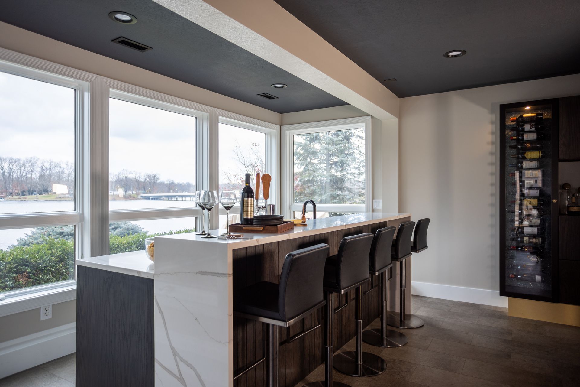 Modern bar with marble countertop, bar stools, and window overlooking a body of water.