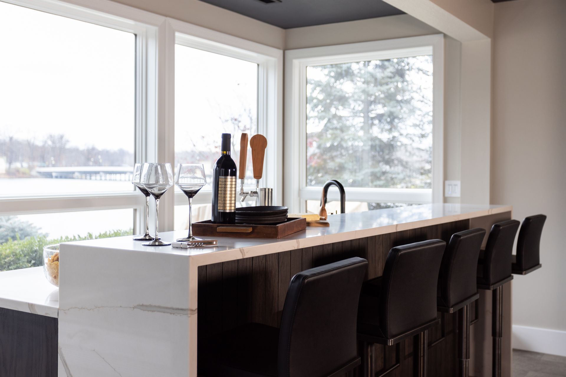 Bar with stools and wine glasses by a window with an outside view.