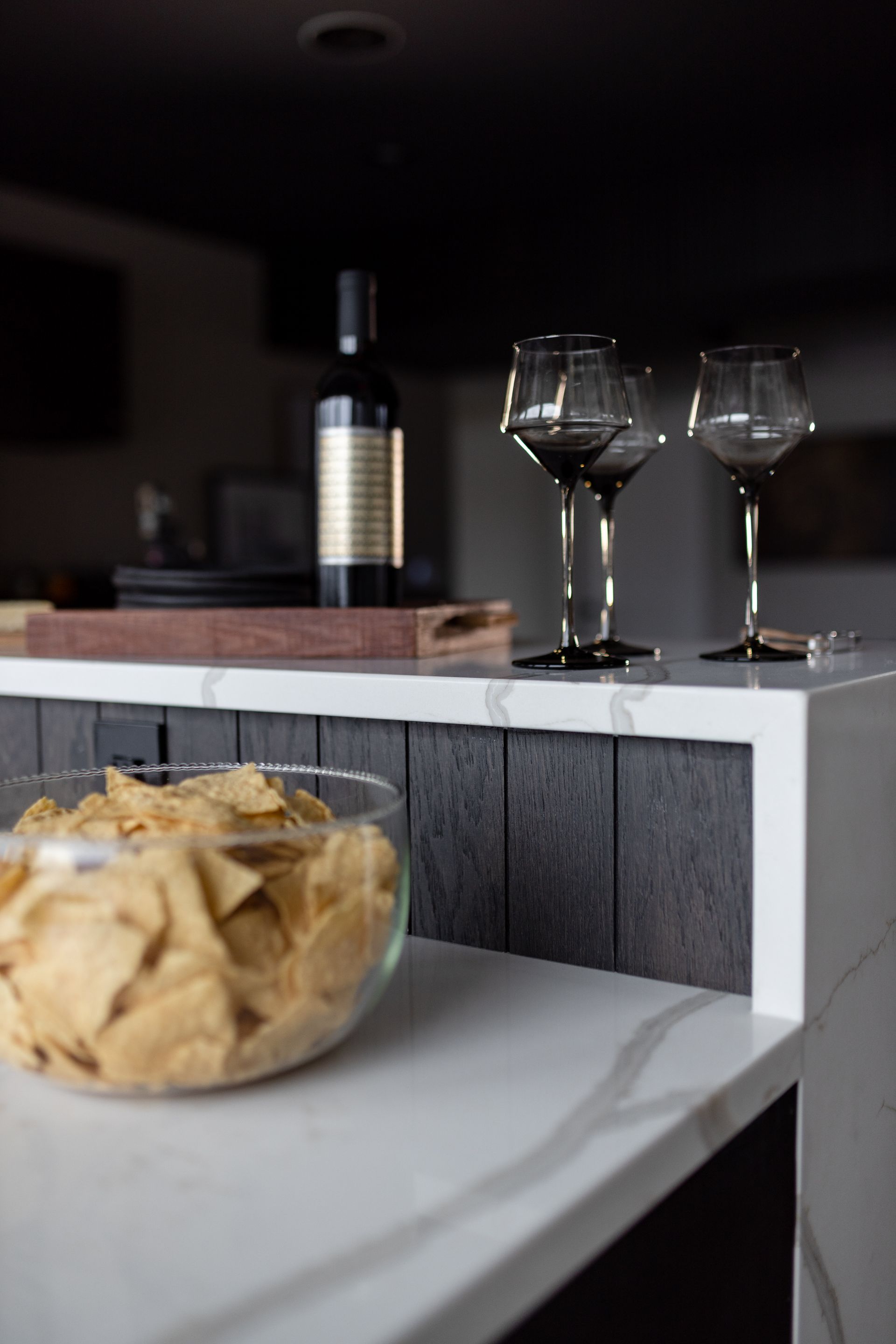Chips, wine glasses, and a bottle on a kitchen counter.