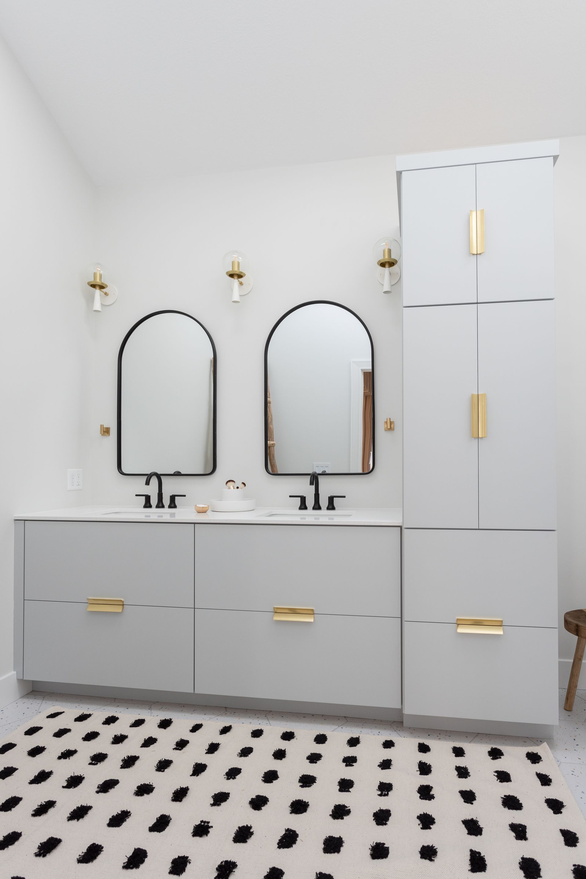 Bathroom with gray vanity, black mirrors, gold accents, and a black and white rug.