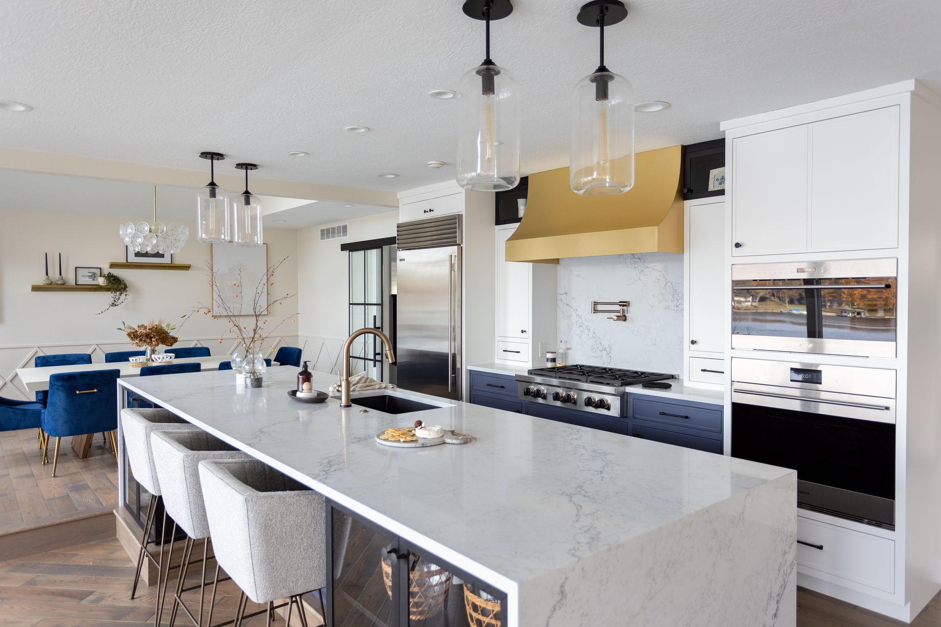 Modern kitchen with white countertops, blue island, gold range hood, and dining area.