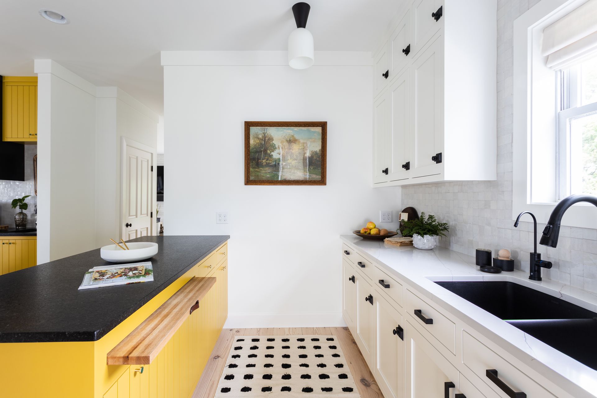 Kitchen with yellow island and white cabinets, black countertops, and a painting on the wall.