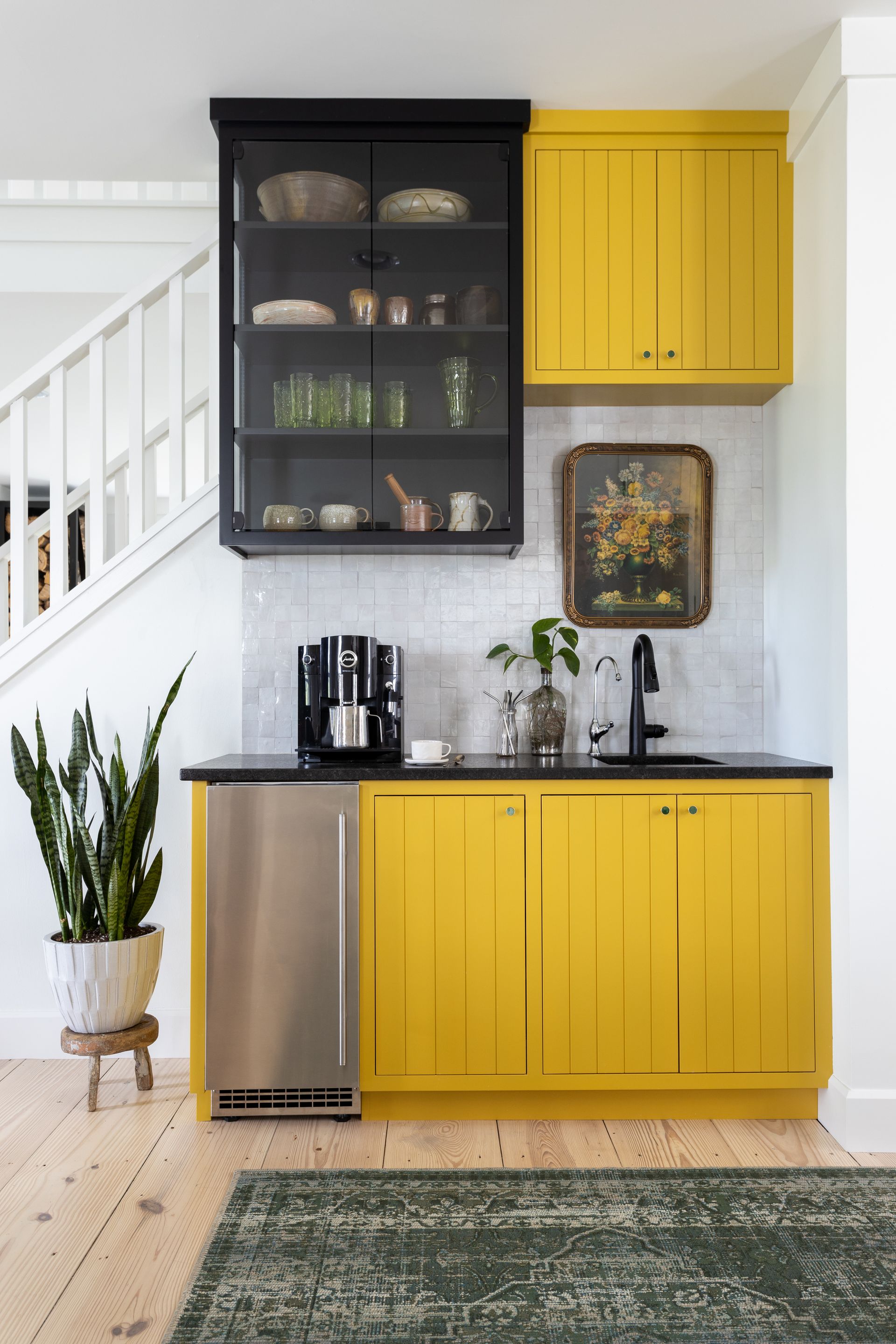 Yellow and black wet bar with stainless steel fridge, glass-front cabinet, and marble backsplash.