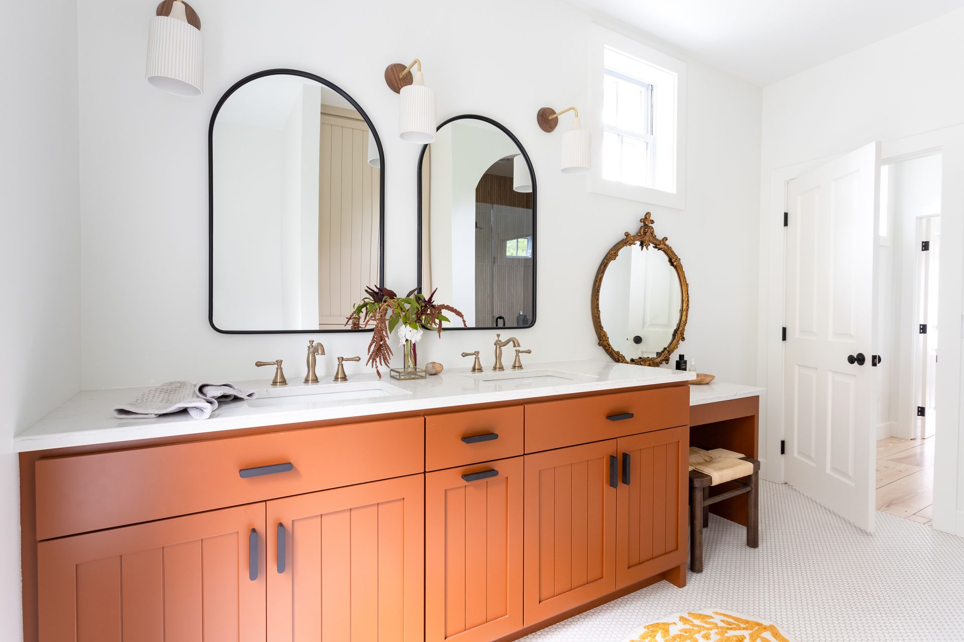 Bathroom with orange vanity, arched mirrors, and a small vanity table.