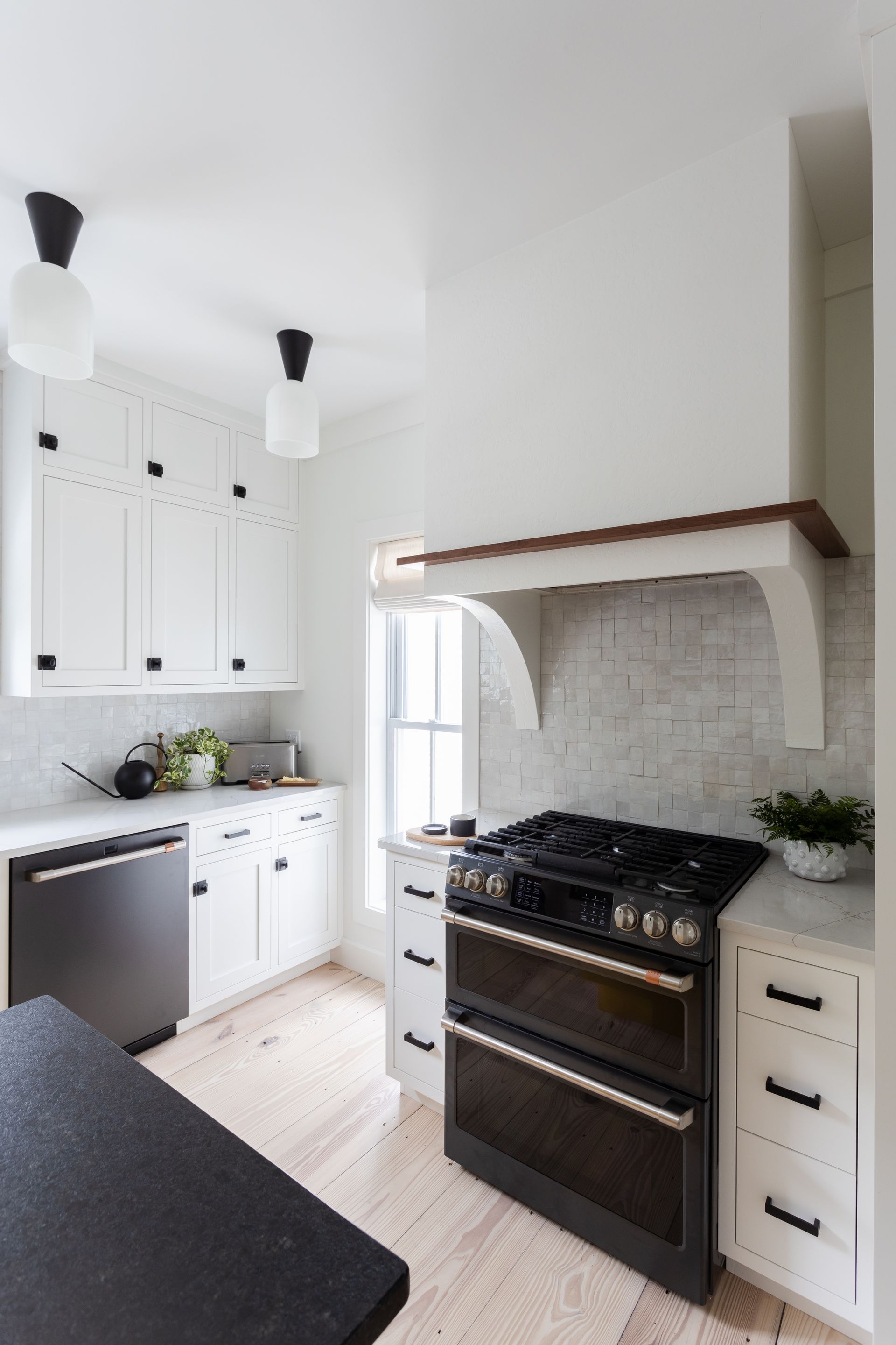 White kitchen with black accents, black double oven, and wood-toned range hood.