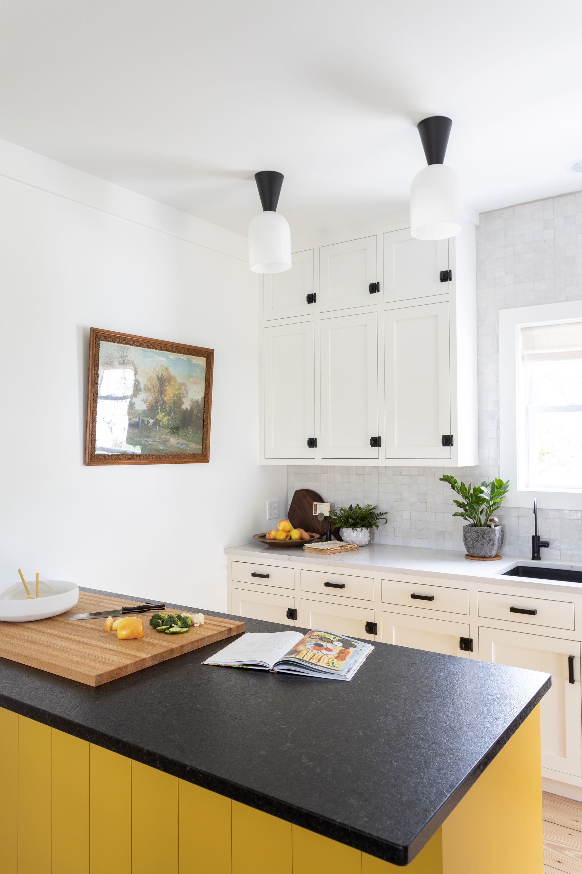 Yellow and black kitchen island with black countertop, white cabinets, and artwork.
