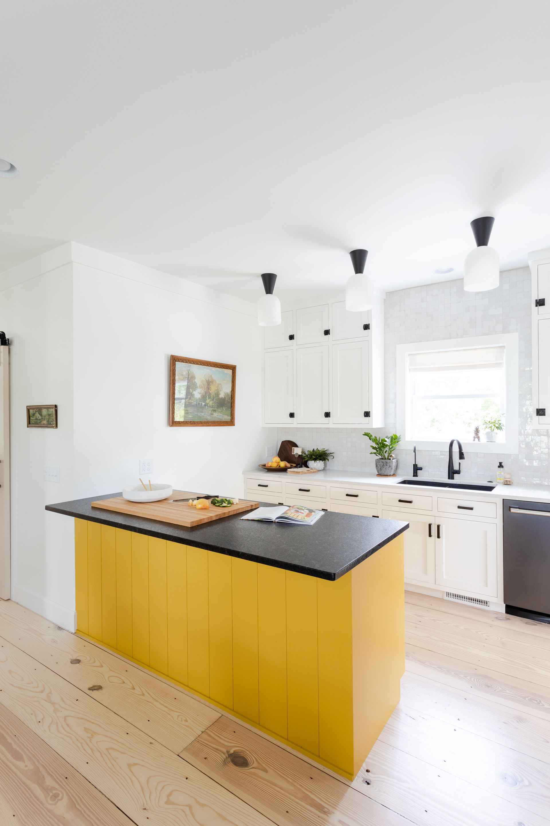 Yellow kitchen island with black countertop in a white kitchen with wood floors.