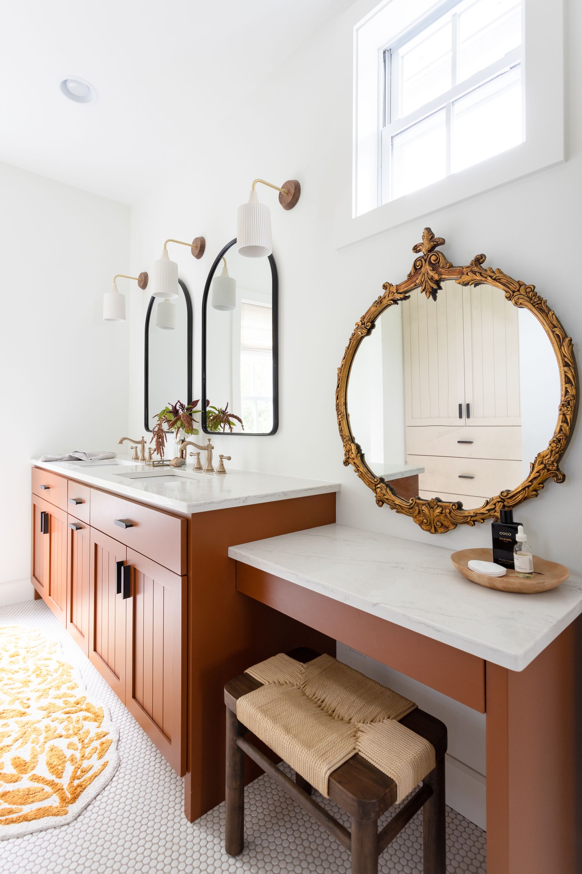 Bathroom with vanity, mirrors, and a wooden cabinet. The space is light, with a patterned rug and warm accents.