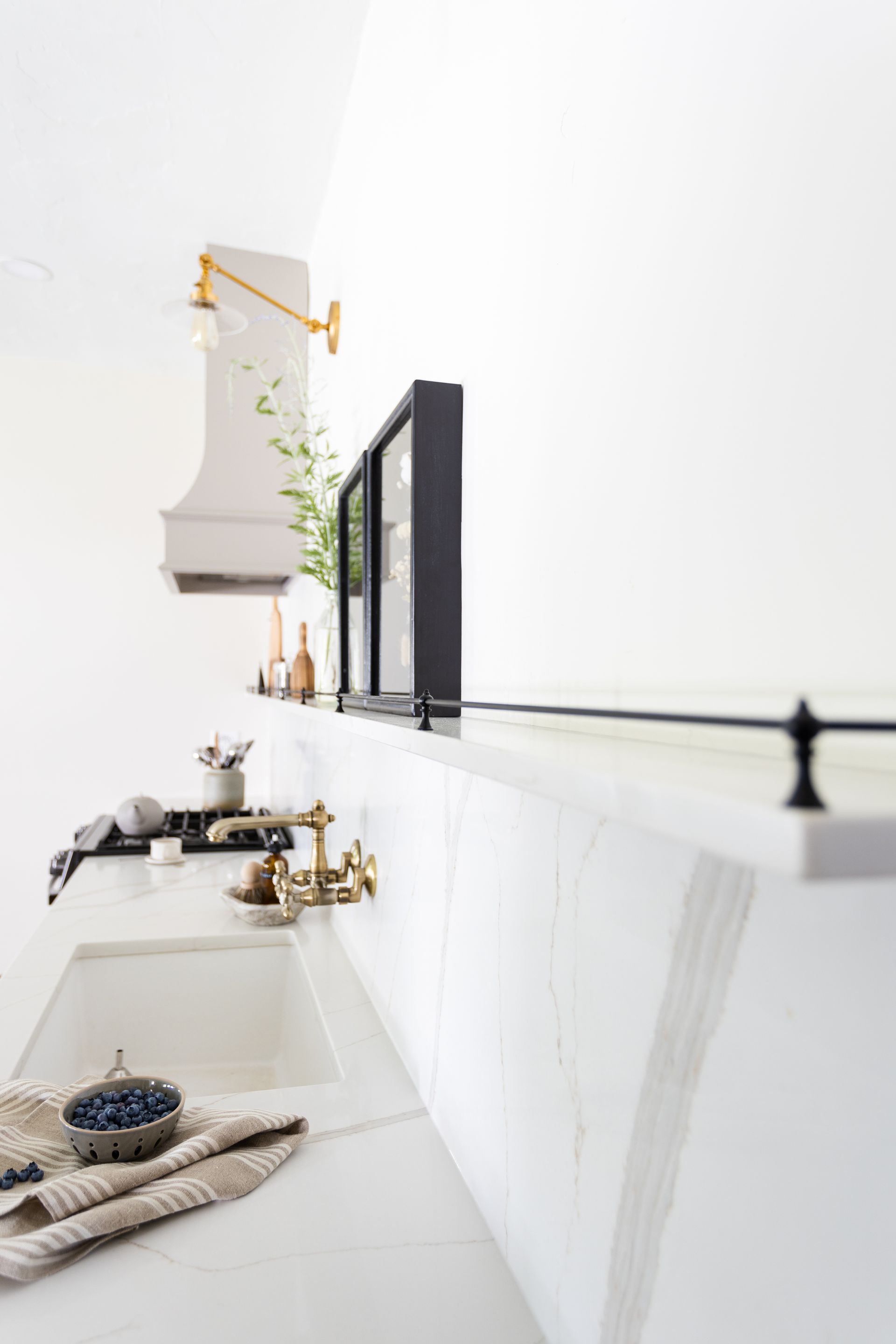 Modern white kitchen with marble countertops, black framed cabinets, and gold fixtures.