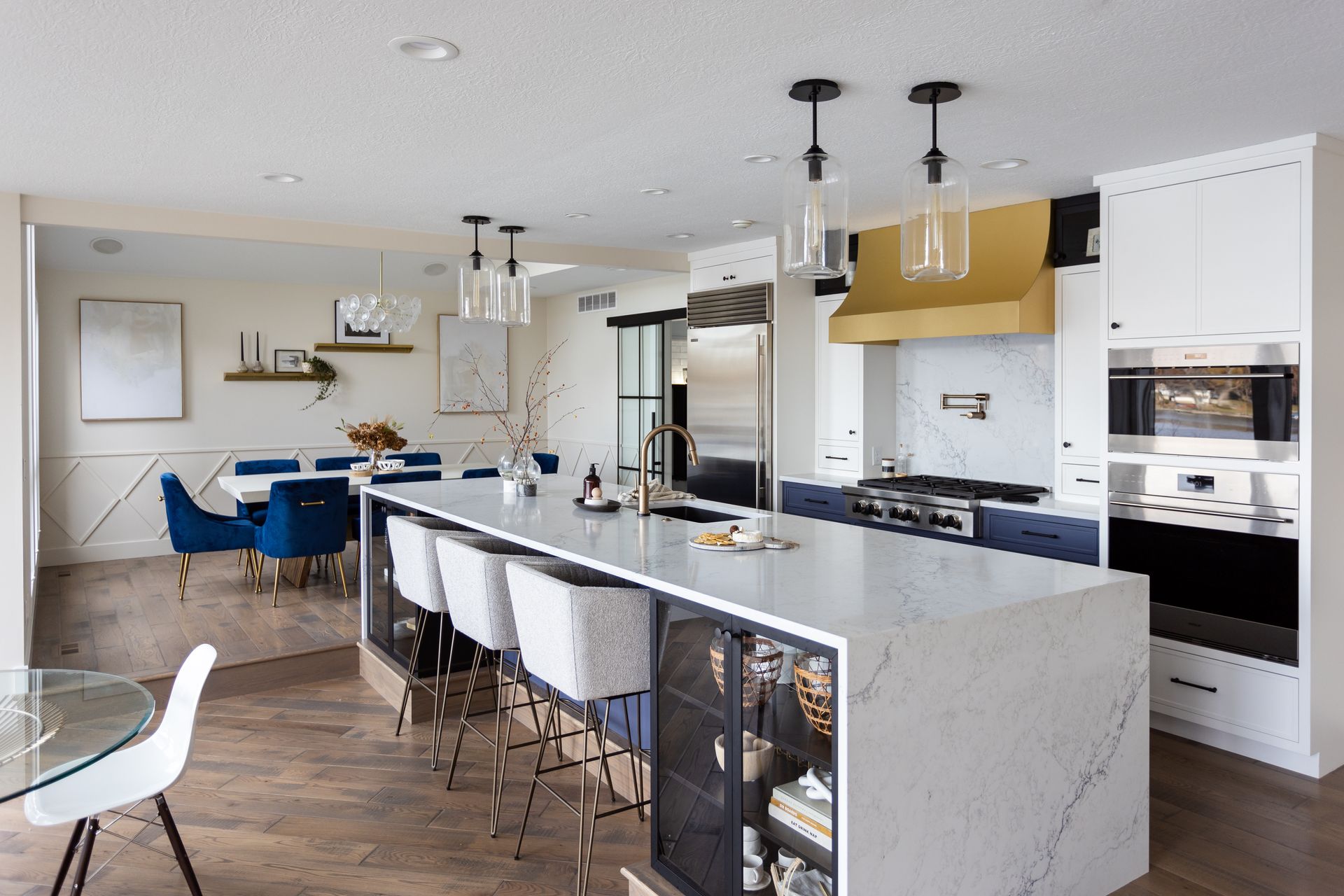 Modern kitchen with large island, marble countertop, gold range hood, and dining area.