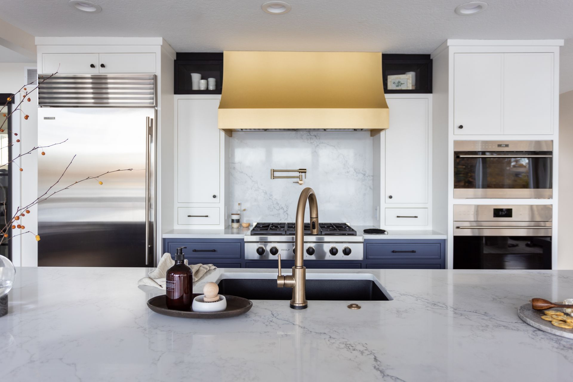 Modern kitchen with white cabinets, gold range hood, marble backsplash, and stainless steel appliances.