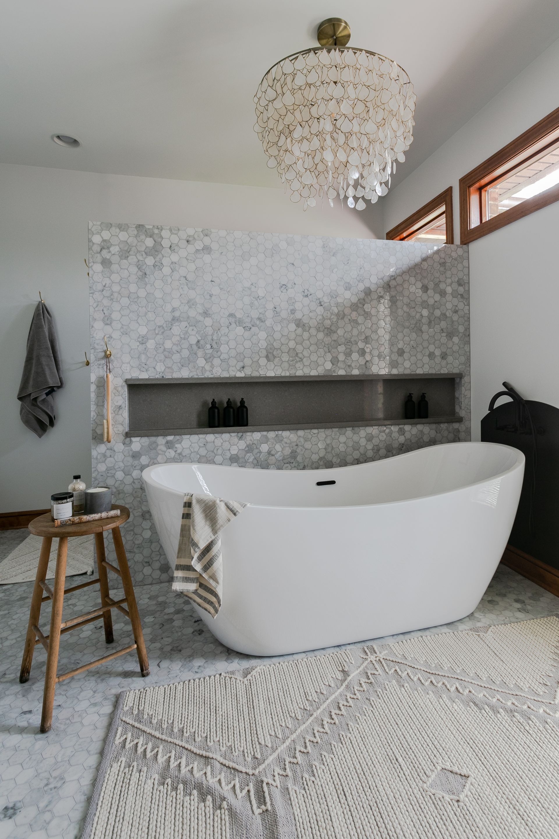 White bathtub in a modern bathroom with a mosaic tiled wall and chandelier.