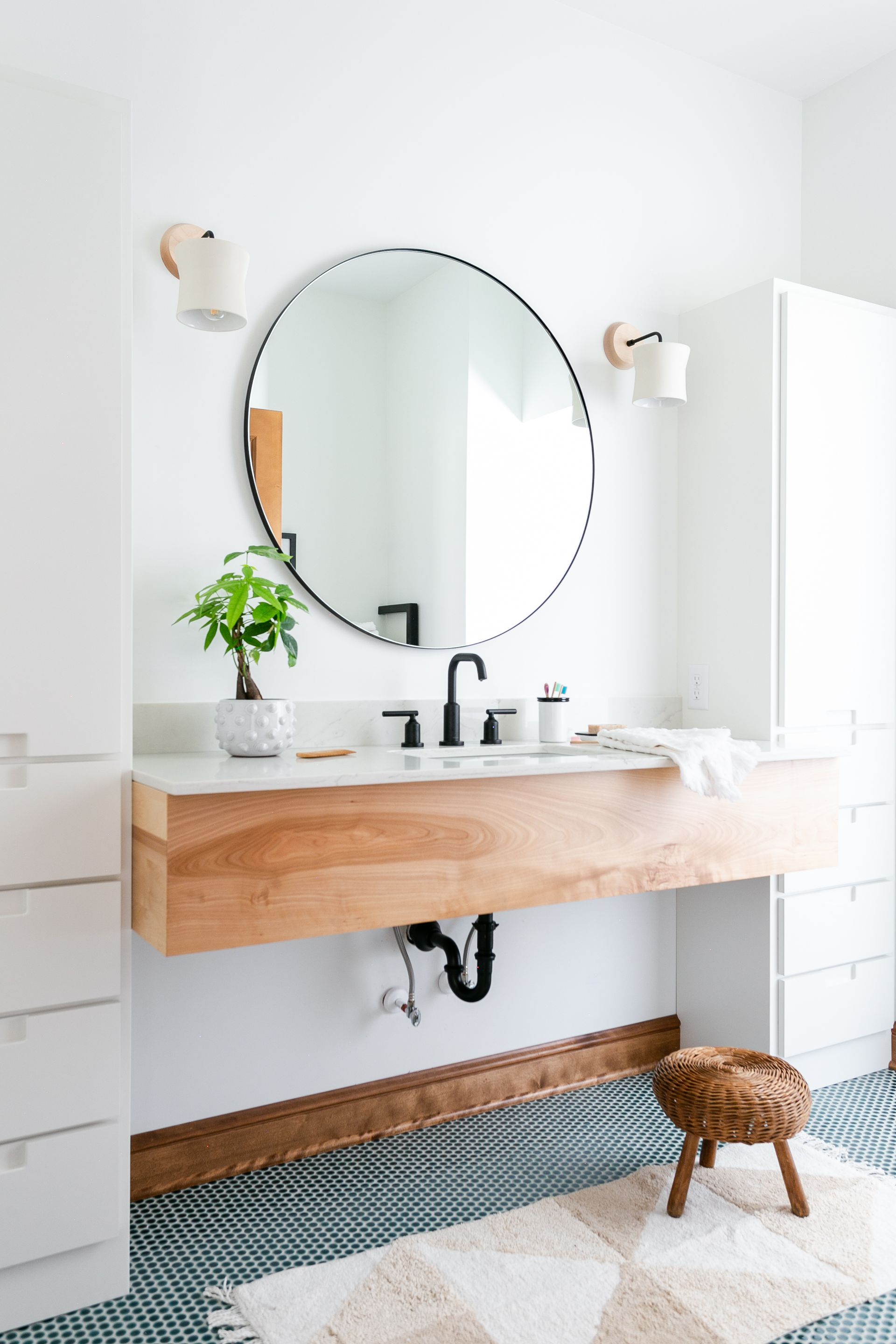 Modern bathroom with a round mirror, floating wood vanity, and black fixtures.