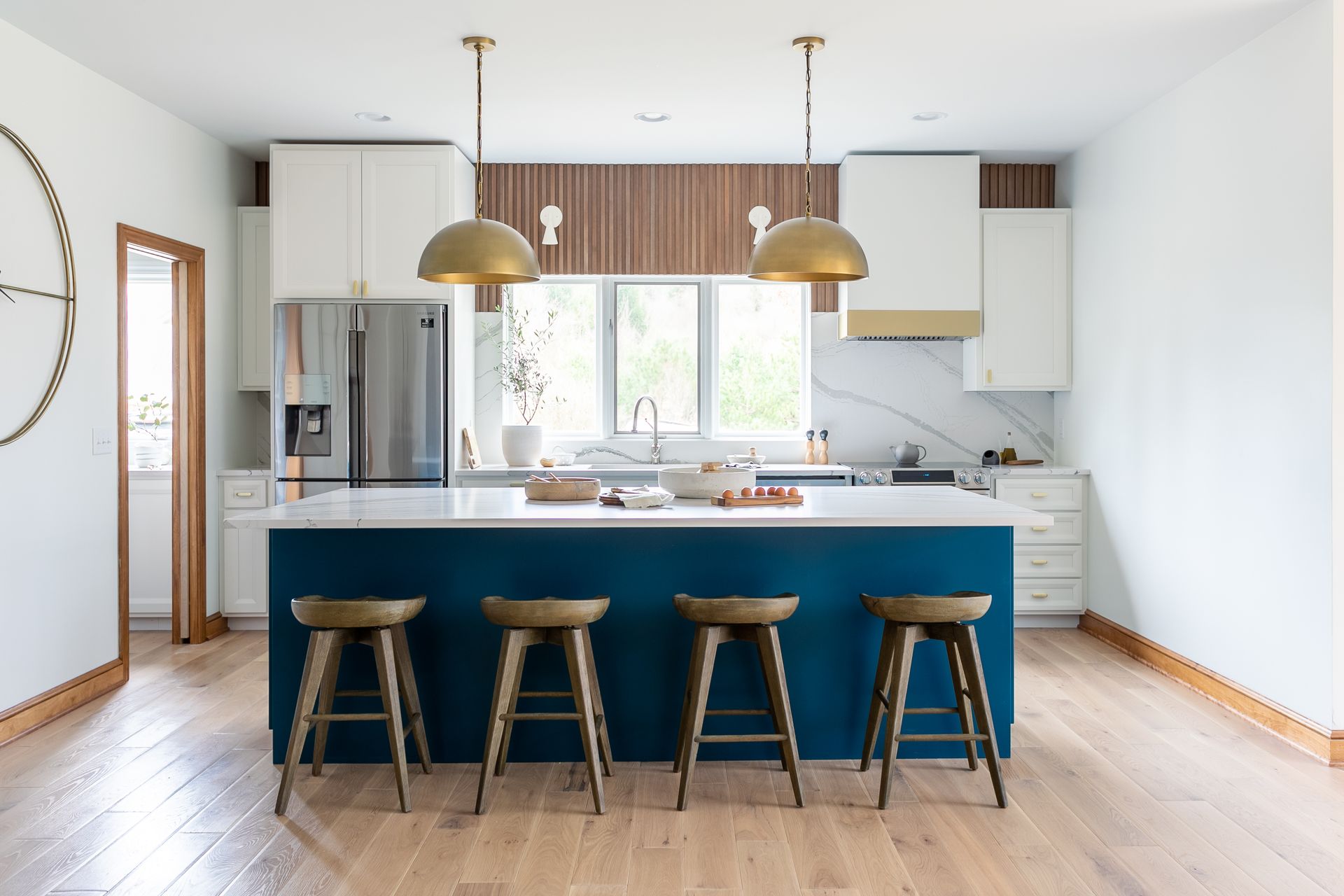 Modern kitchen with blue island and gold accents, four bar stools, and pendant lights.