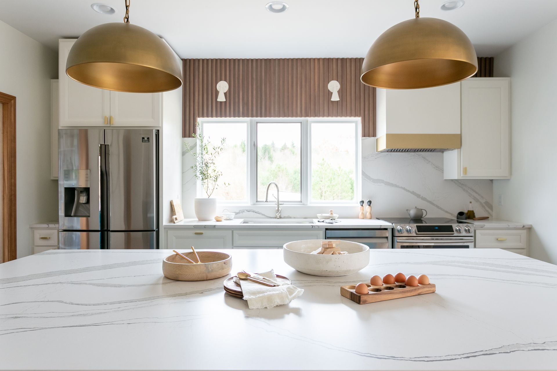 Modern kitchen with a white countertop island, stainless steel appliances, and gold pendant lights.
