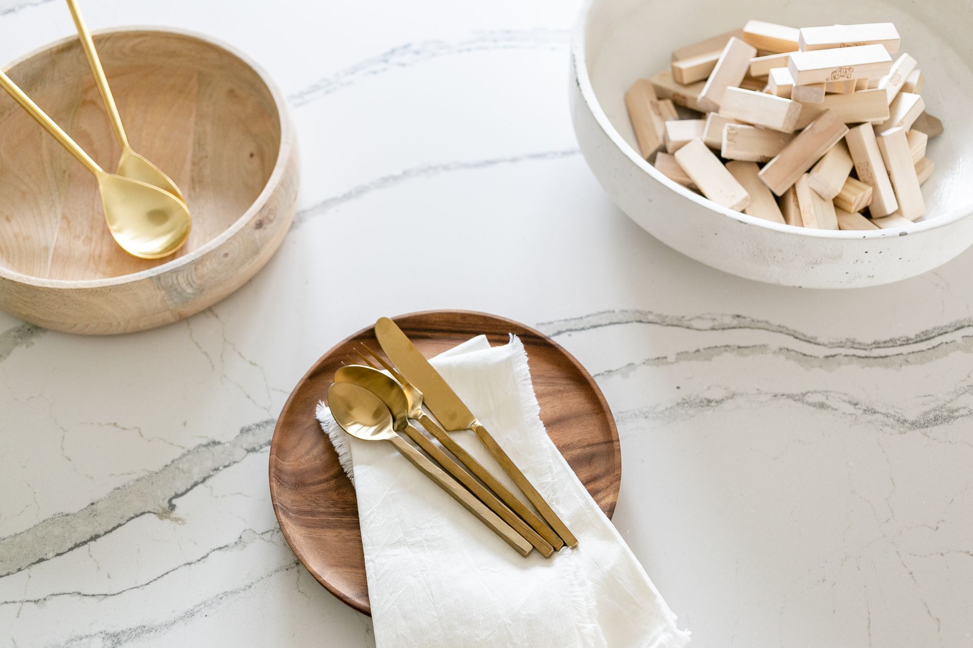 Wooden bowls, gold flatware, and a linen napkin arranged on a marbled surface.