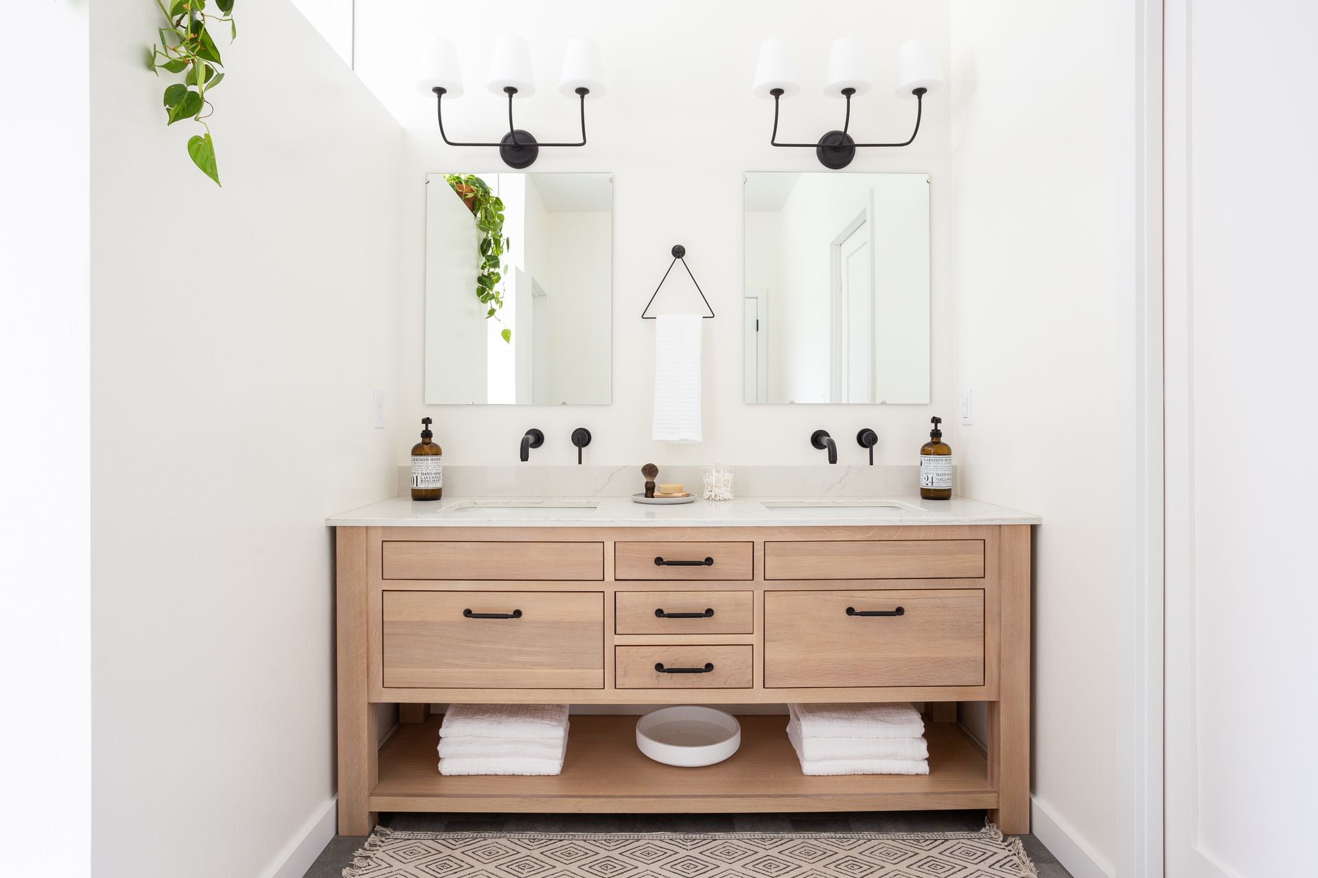 Modern bathroom with double vanity, light wood cabinets, and black fixtures.