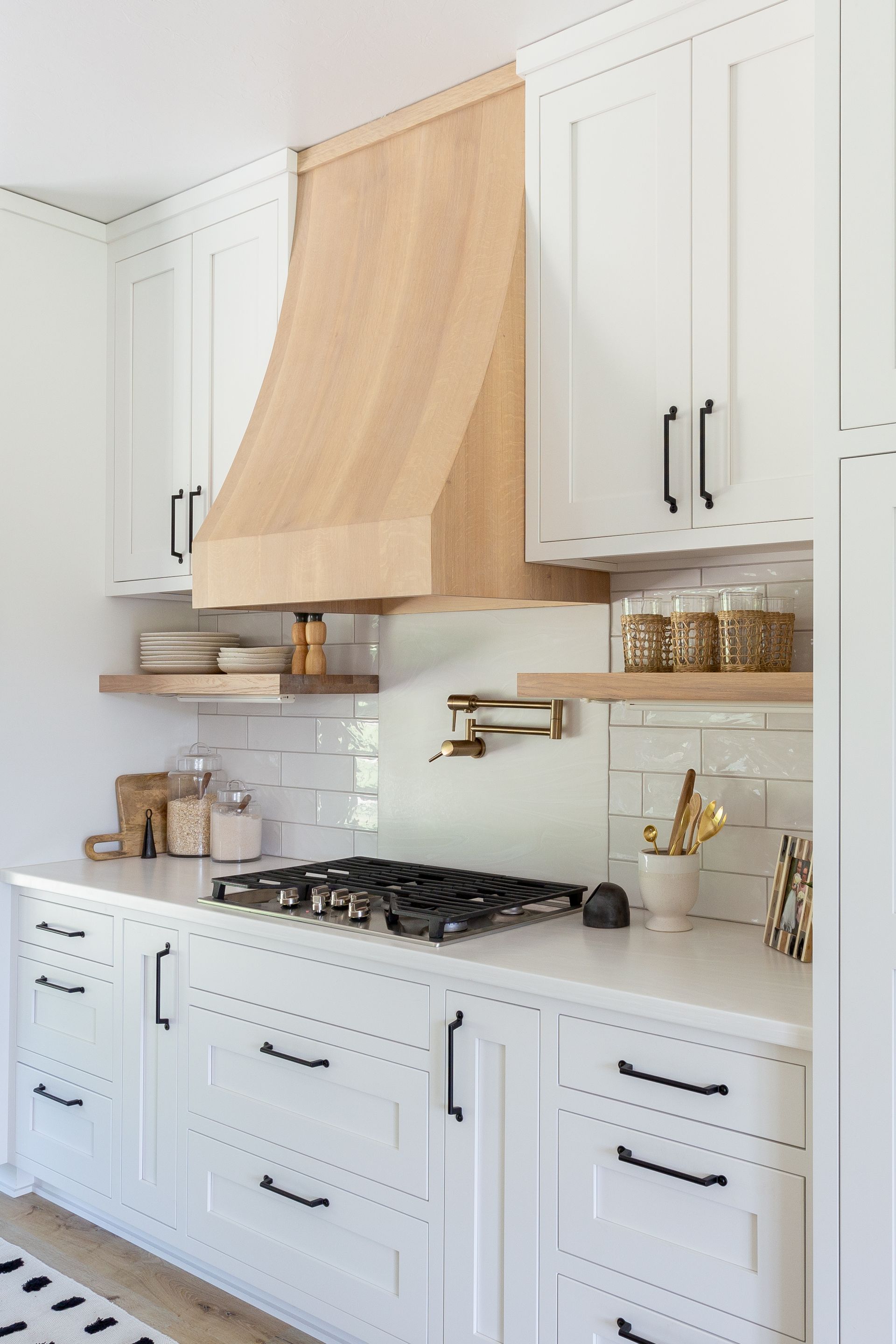 White kitchen with a light wood range hood, white cabinets, and gas stovetop.