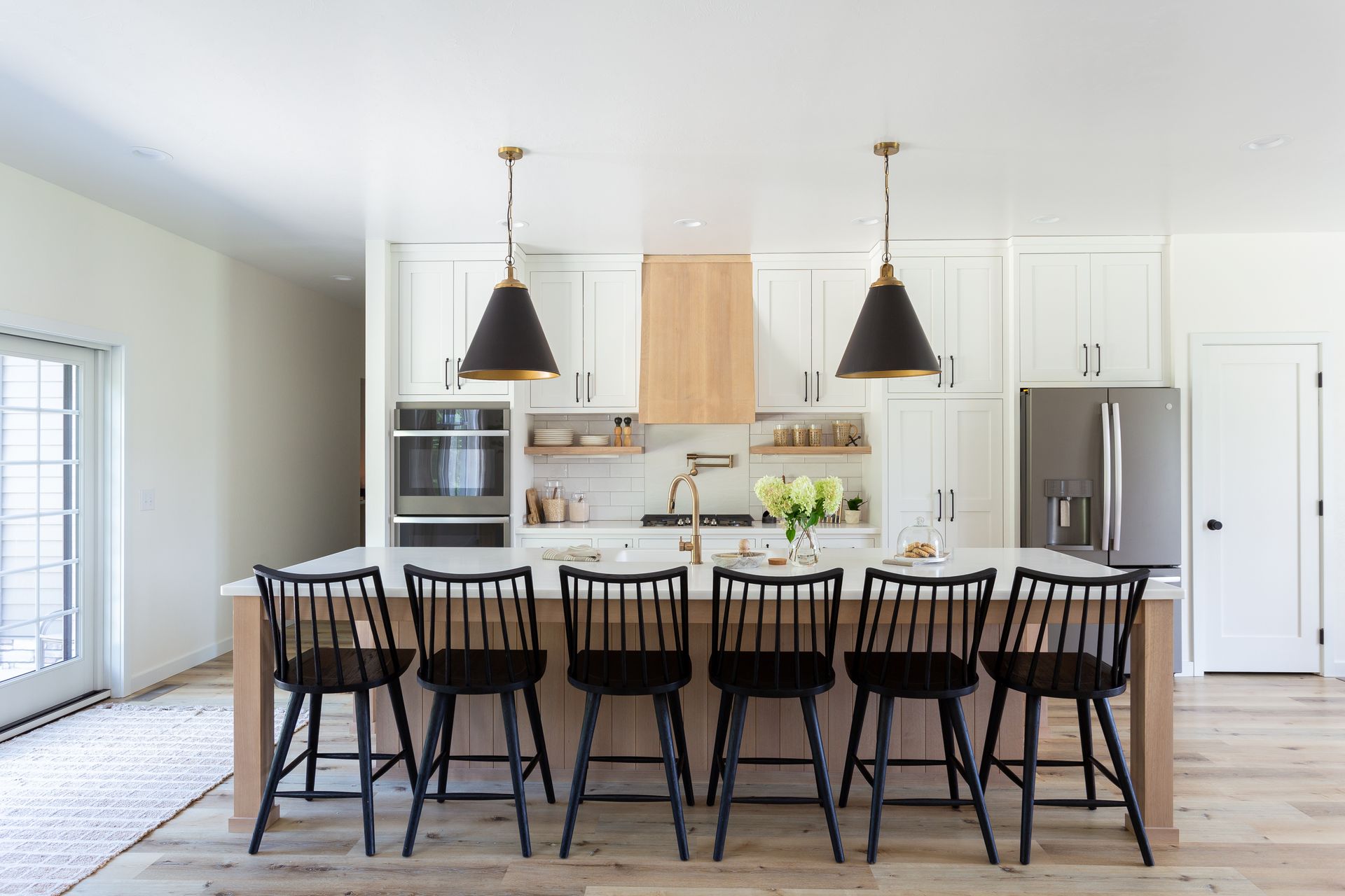 Modern kitchen with white cabinets, wood accents, black chairs, and pendant lights.