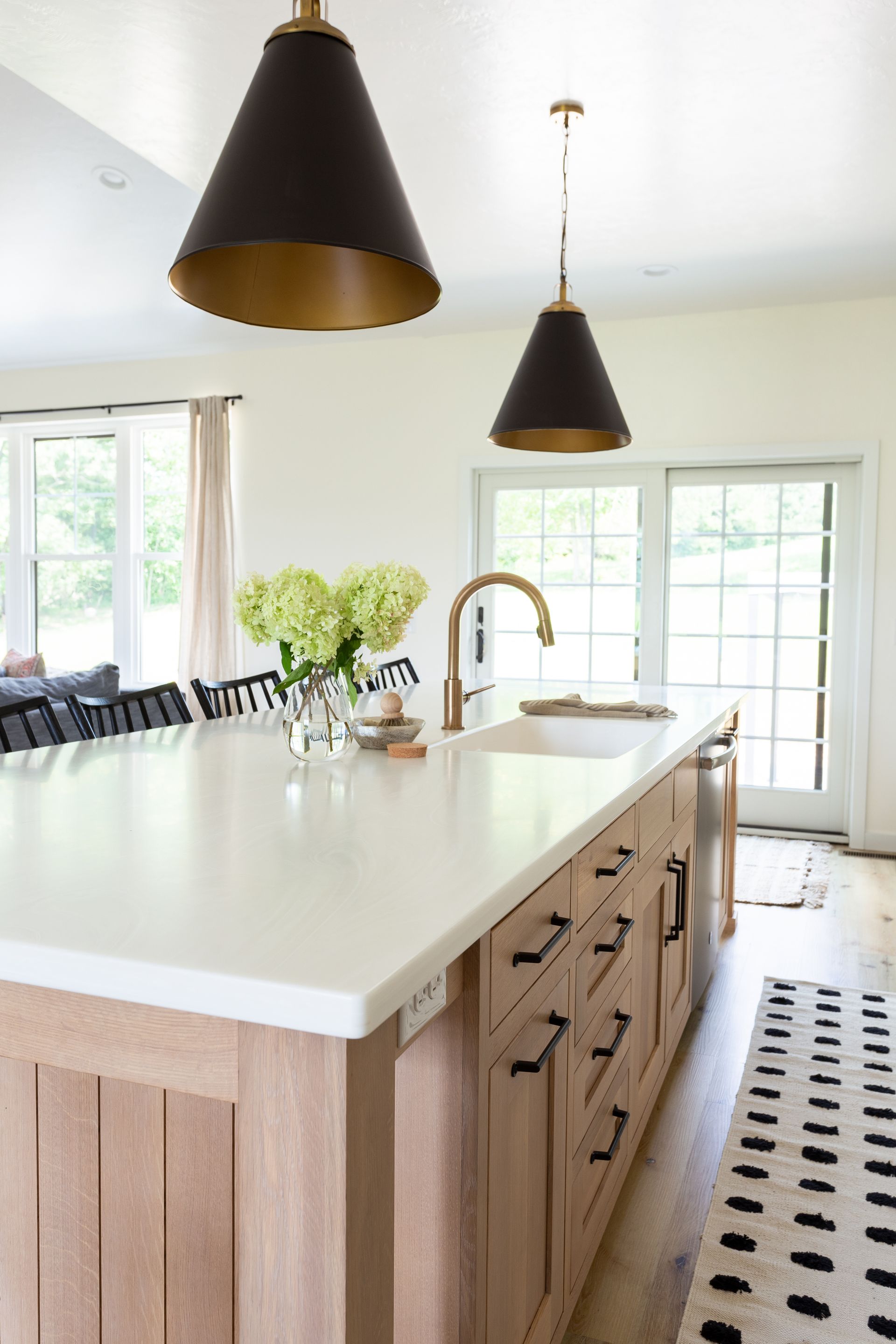 Kitchen island with white countertop, wooden base, black pendant lights, and gold faucet.