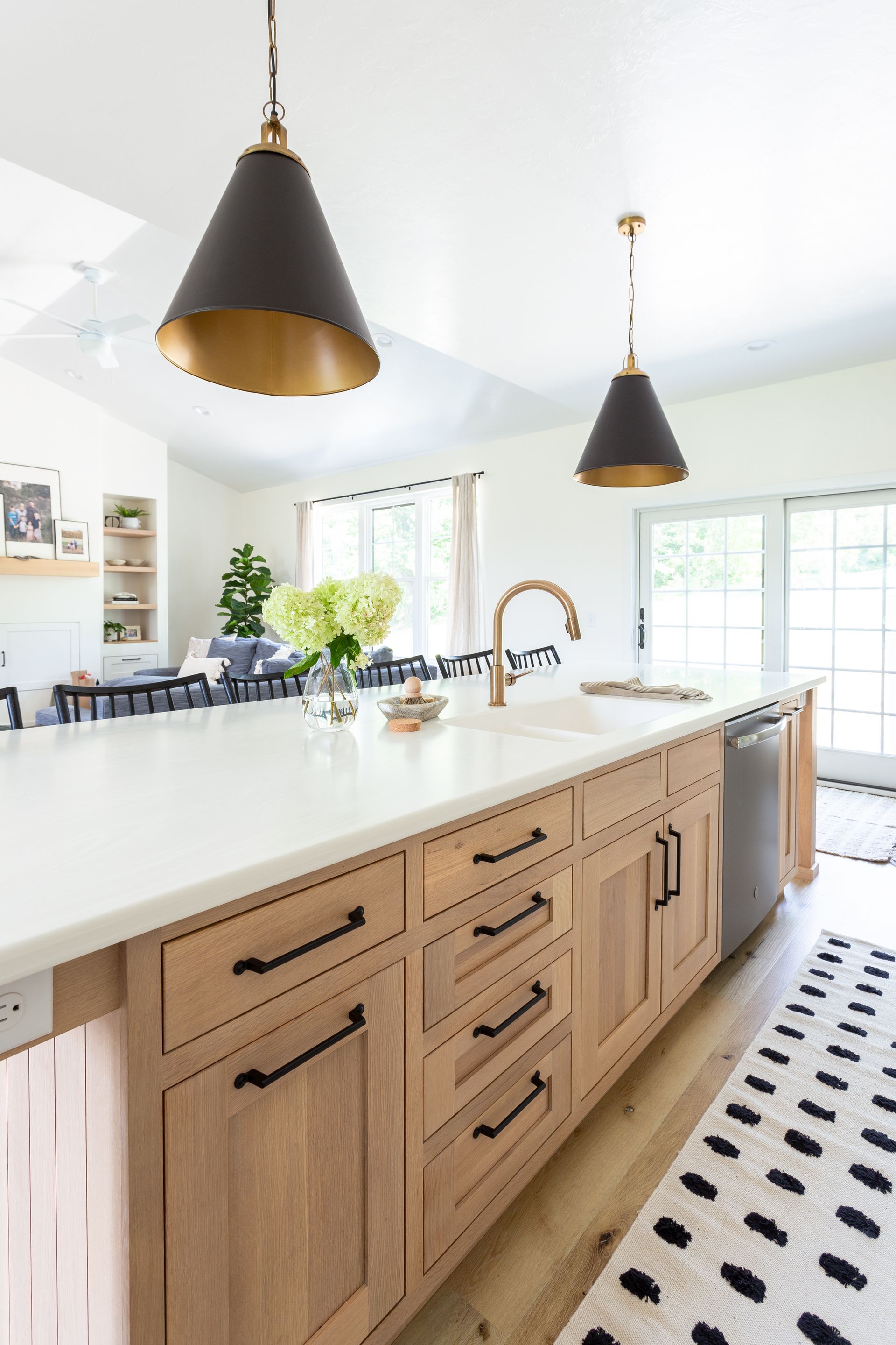 Kitchen island with light wood cabinets, white countertop, and gold pendant lights.