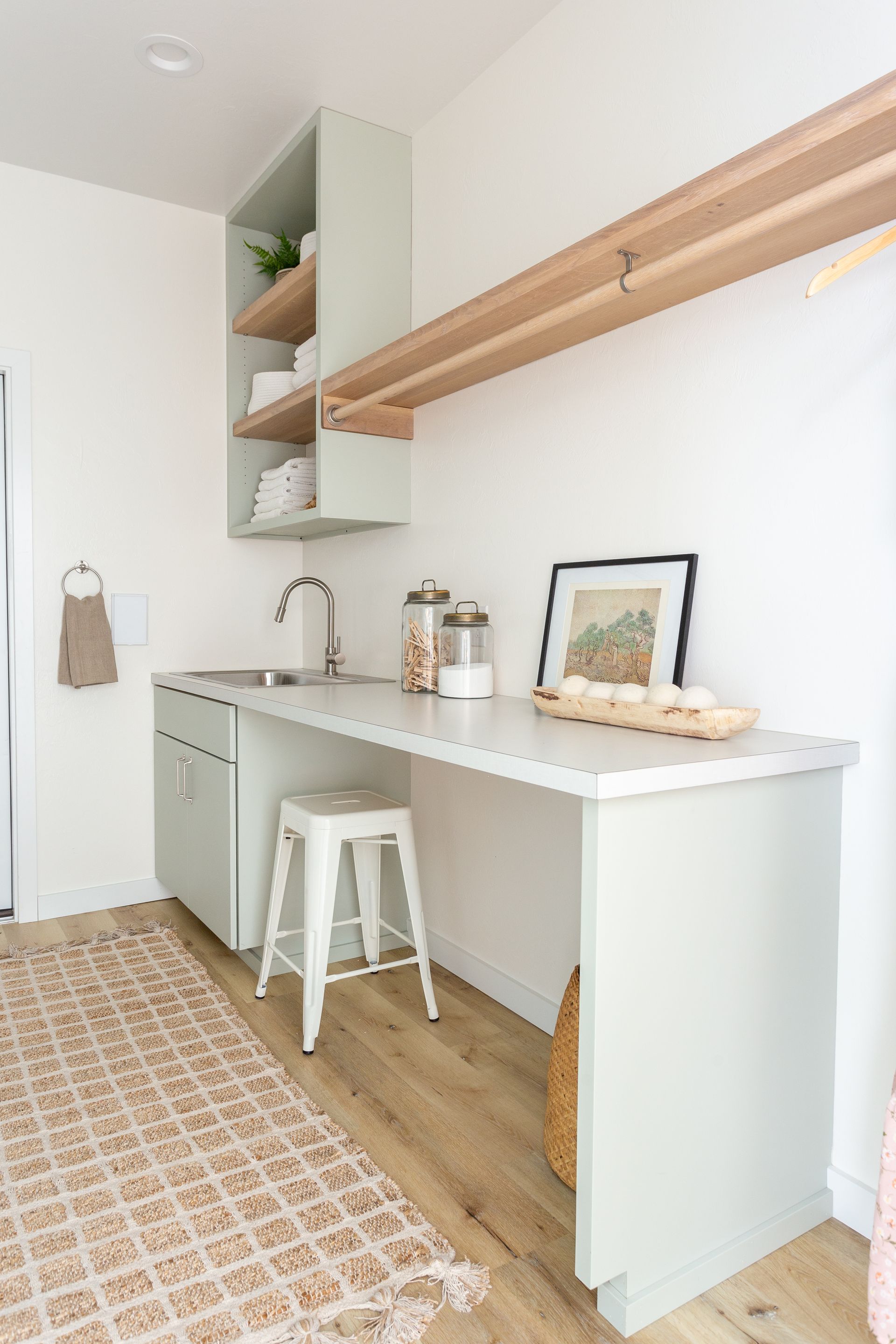 Laundry room with green cabinetry, a white countertop, and wooden drying rack. A tan rug is on the floor.