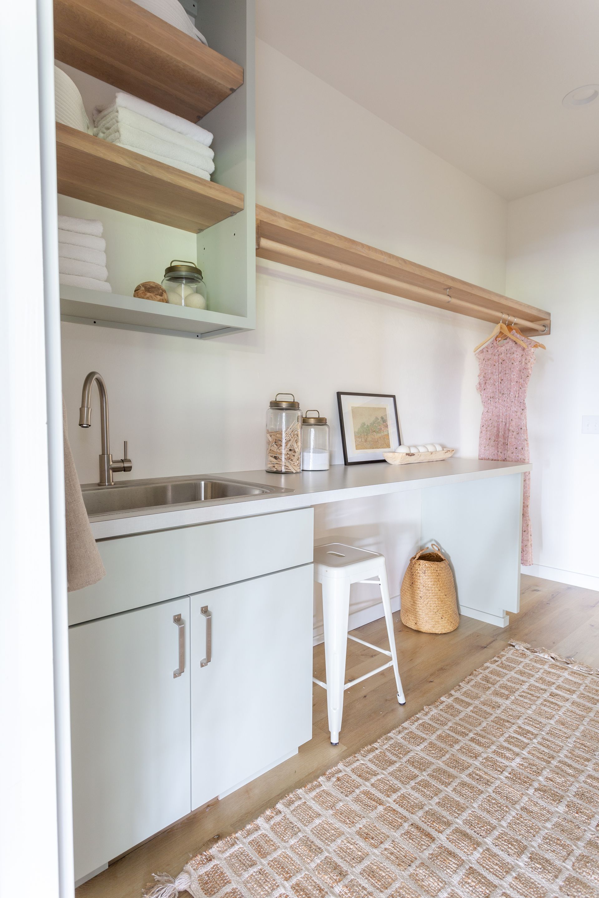 Laundry room with sink, cabinets, open shelving, drying rack, stool, and rug.