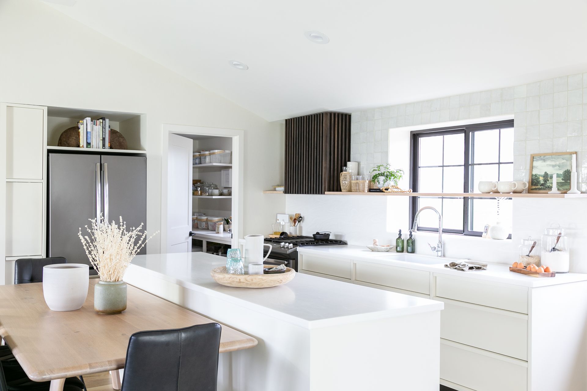 Bright, modern kitchen with white cabinetry, large island, stainless steel refrigerator, and pantry.
