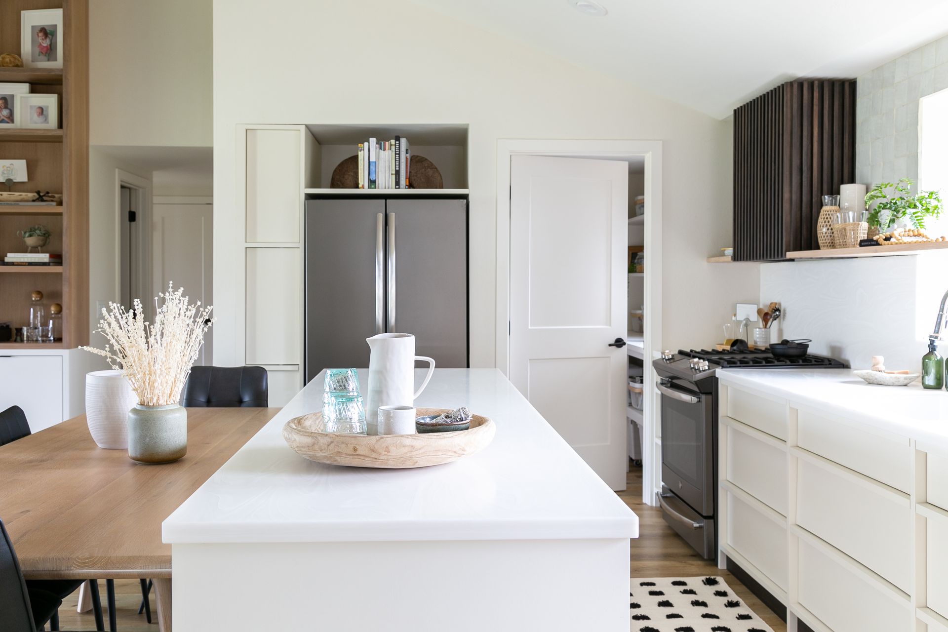 Modern kitchen with island, stainless steel refrigerator, white cabinets, and dark range hood.