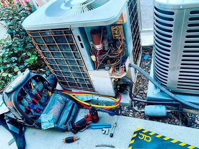 Open HVAC units with exposed wiring and tools on the ground during repair