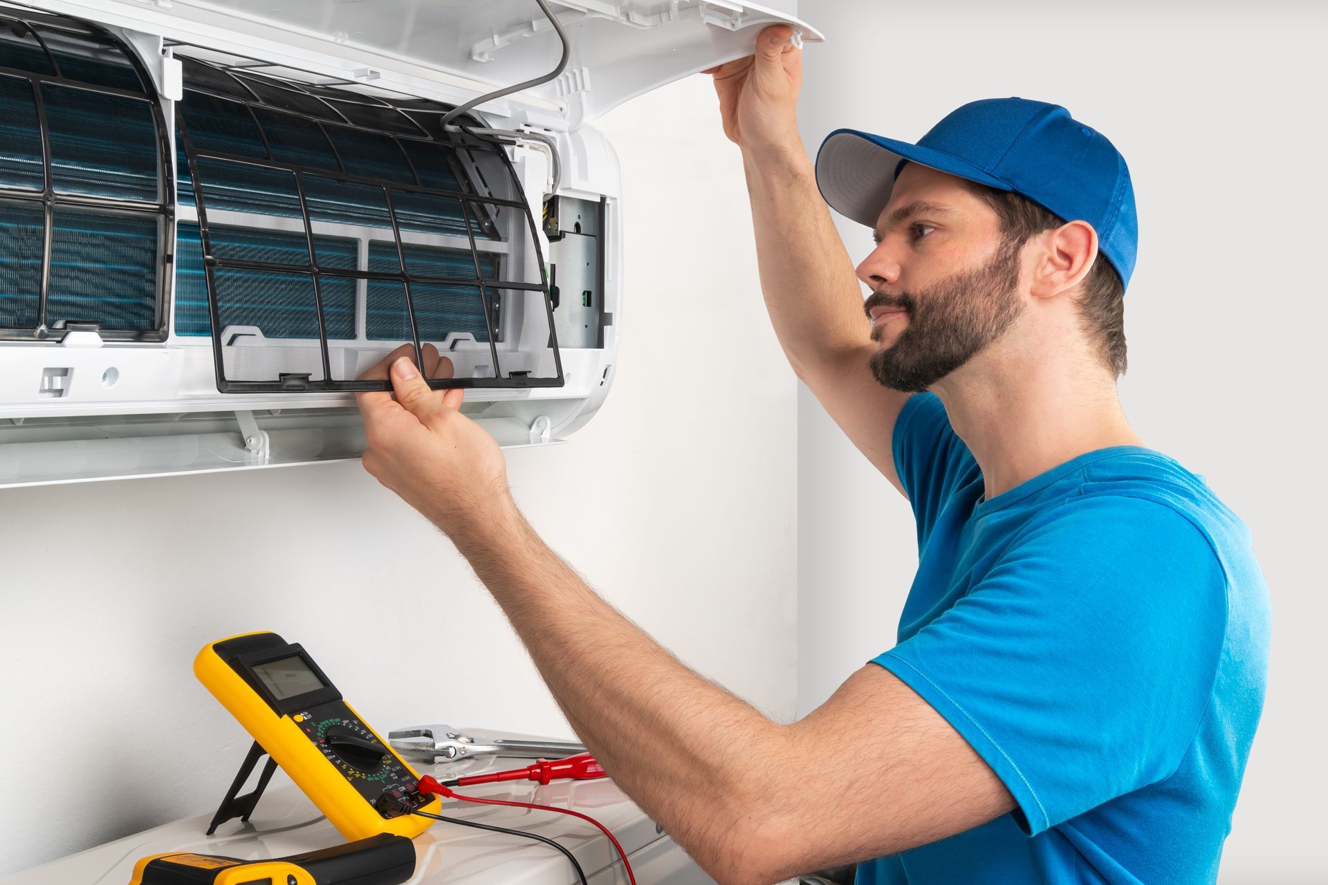 An HVAC technician inspecting an open AC unit with a multimeter on a nearby surface. An HVAC technician inspecting an open AC unit with a multimeter on a nearby surface.